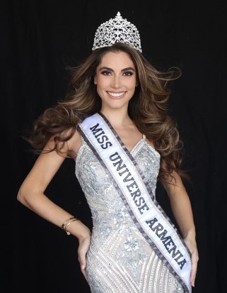 Photo of Kristina Ayanian ’19 in white beaded evening gown, wearing a glittering tiara and sash that reads "Miss Universe Armenia 2022."
