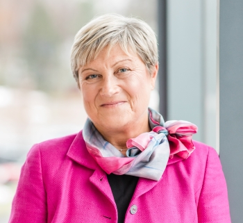 Headshot of Management Professor Tatiana Manolova wearing a bright pink blazer and light grey and pink patterned scarf.