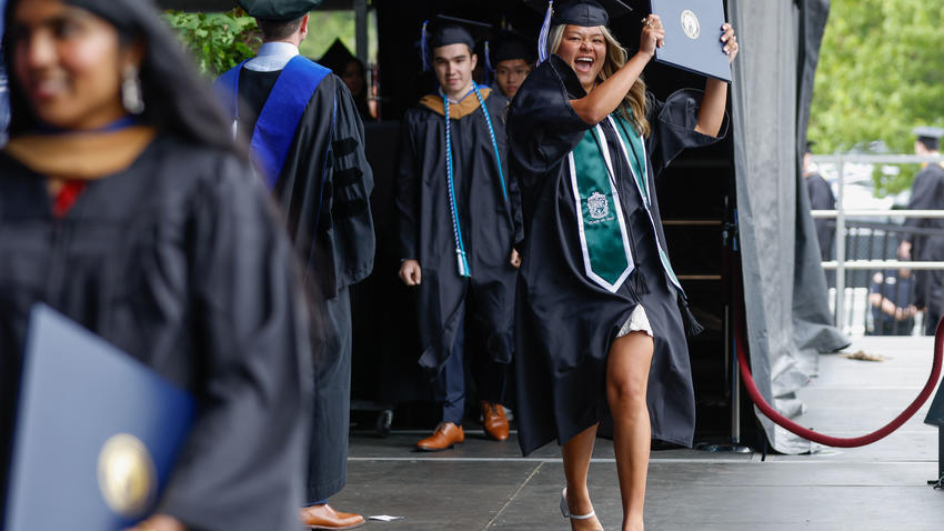 A student holds up her diploma triumphantly as she crosses the stage 