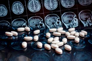 Pile of white pills sitting atop brain scan images