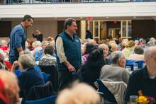 Man smiling amid crowd of people seated for luncheon