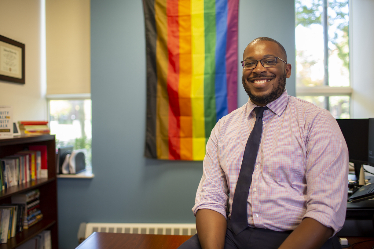 Patrick Couillard Hale in his office with pride flag on wall