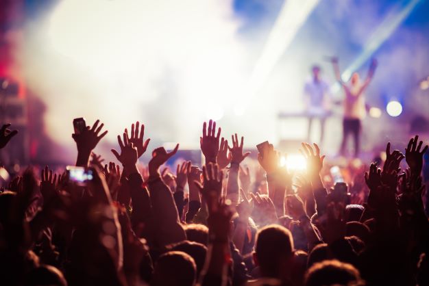 Concert goes with hands waving in the air as they watch performer on stage