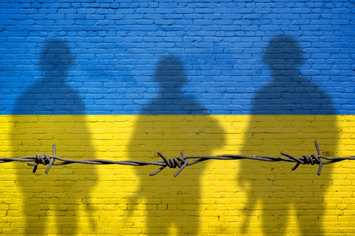 The Ukrainian flag overlaid with the shadows of three soldiers and a strand of barbed wire.