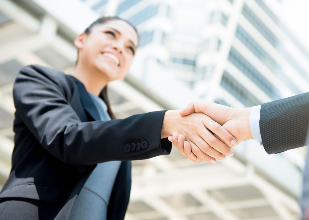 Person wearing a suit shaking a hand in front of a building