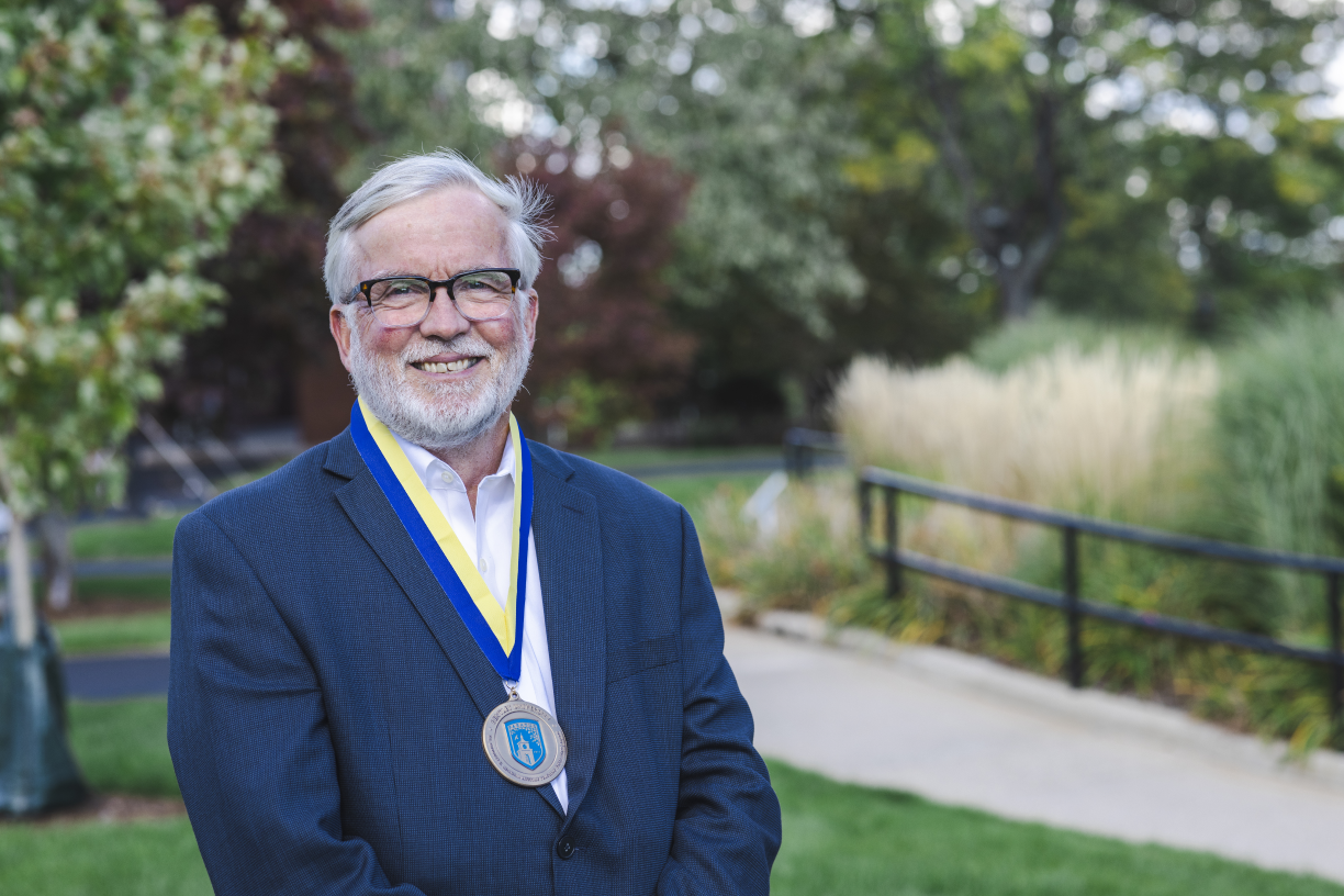 Professor Bill Gribbons poses with the medal for the 2022 Adamian Award for Lifetime Teaching Excellence on a ribbon around his neck.
