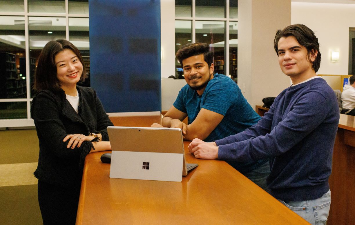 Graduate students Alice Zhang, Abhijit Chandrasekhar and Jose Ordaz stand around a laptop computer in the Bentley Library.