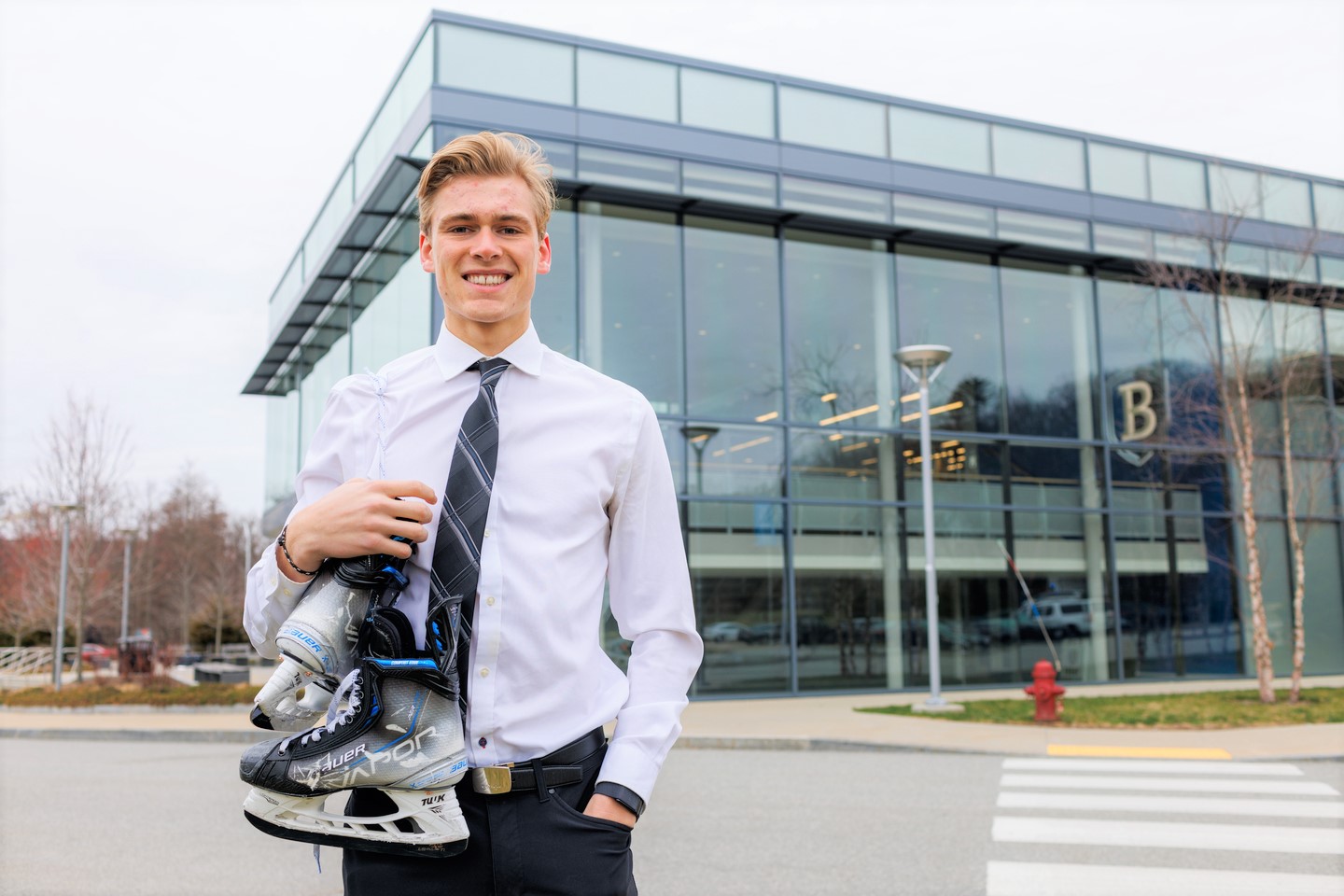 Lucas Vanroboys standing in front of the Bentley Arena with hockey skates draped over his shoulder