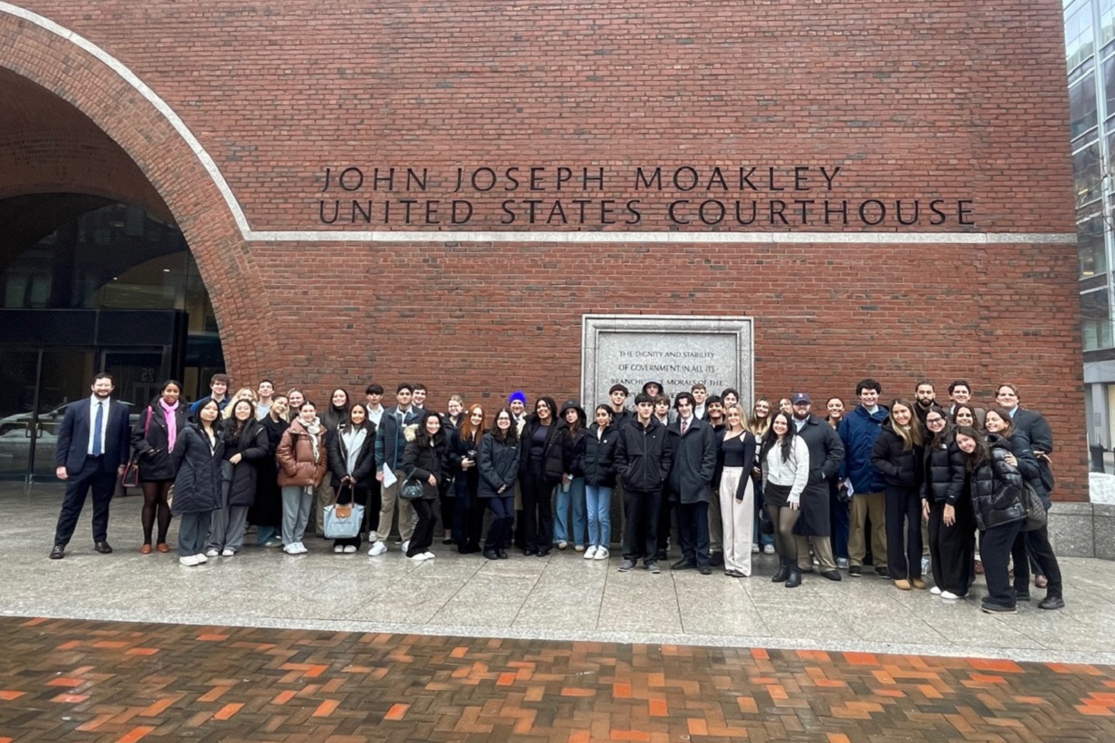 Roughly 50 Bentley students and their faculty chaperones pose outside the brick facade of the John Joseph Moakley U.S. Courthouse in Boston.