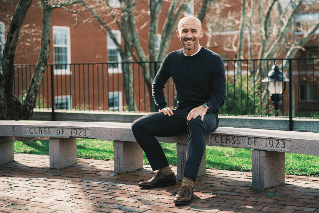 Economics professor sits on a curved concrete bench engraved with "Class of 1923."
