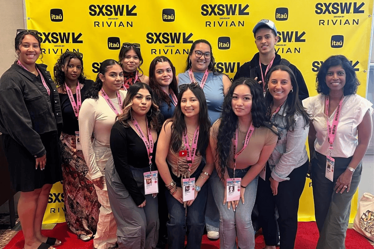 Eleven first generation students pose with Bentley staff member Neelangi Gunasakera in front of a yellow step-and-repeat banner during the 2025 SXSW conference.