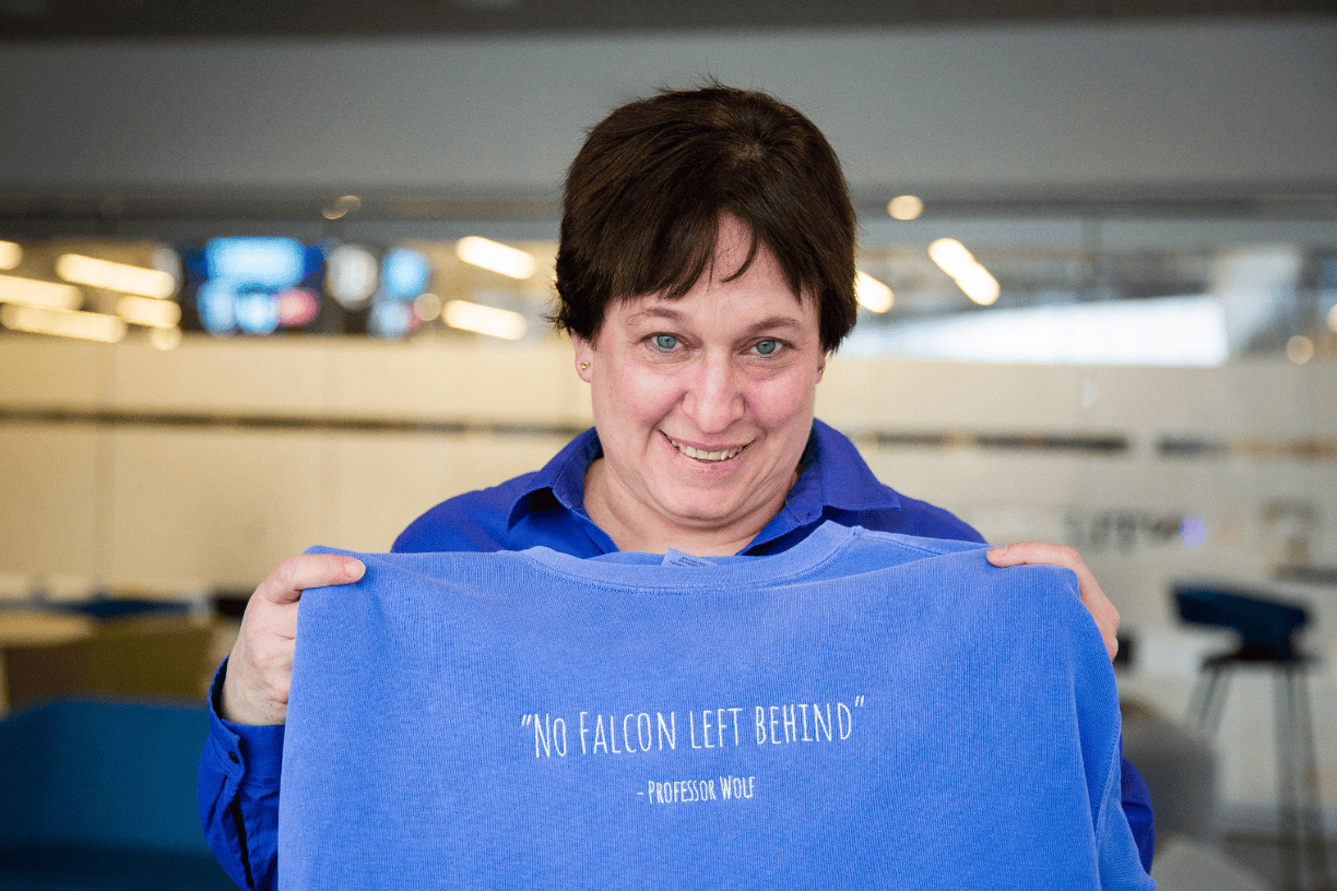 Lecturer in Accounting Lynn Wolf hods a blue sweatshirt embroidered with her name and the words "No Falcon Left Behind."