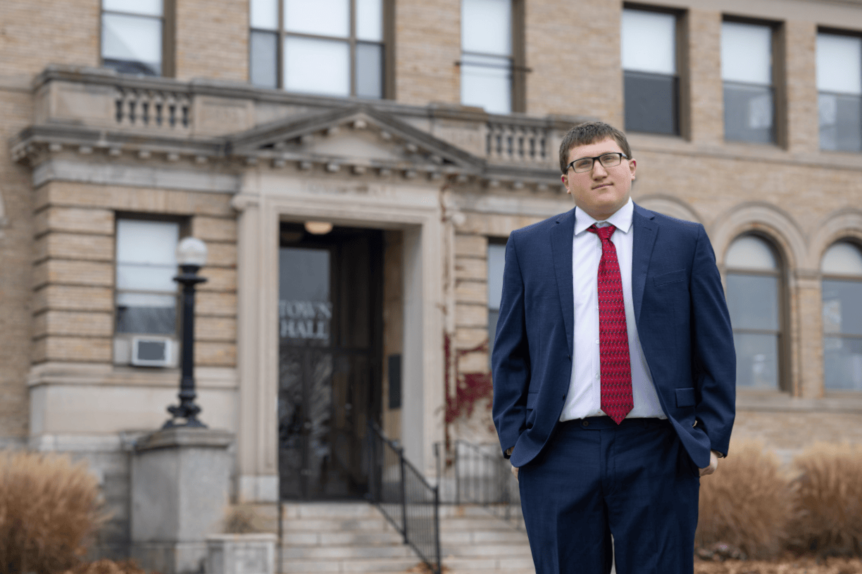 Joe Romano stands in front of Winthrop's Town Hall wearing a navy blue suit, white shirt and red tie.