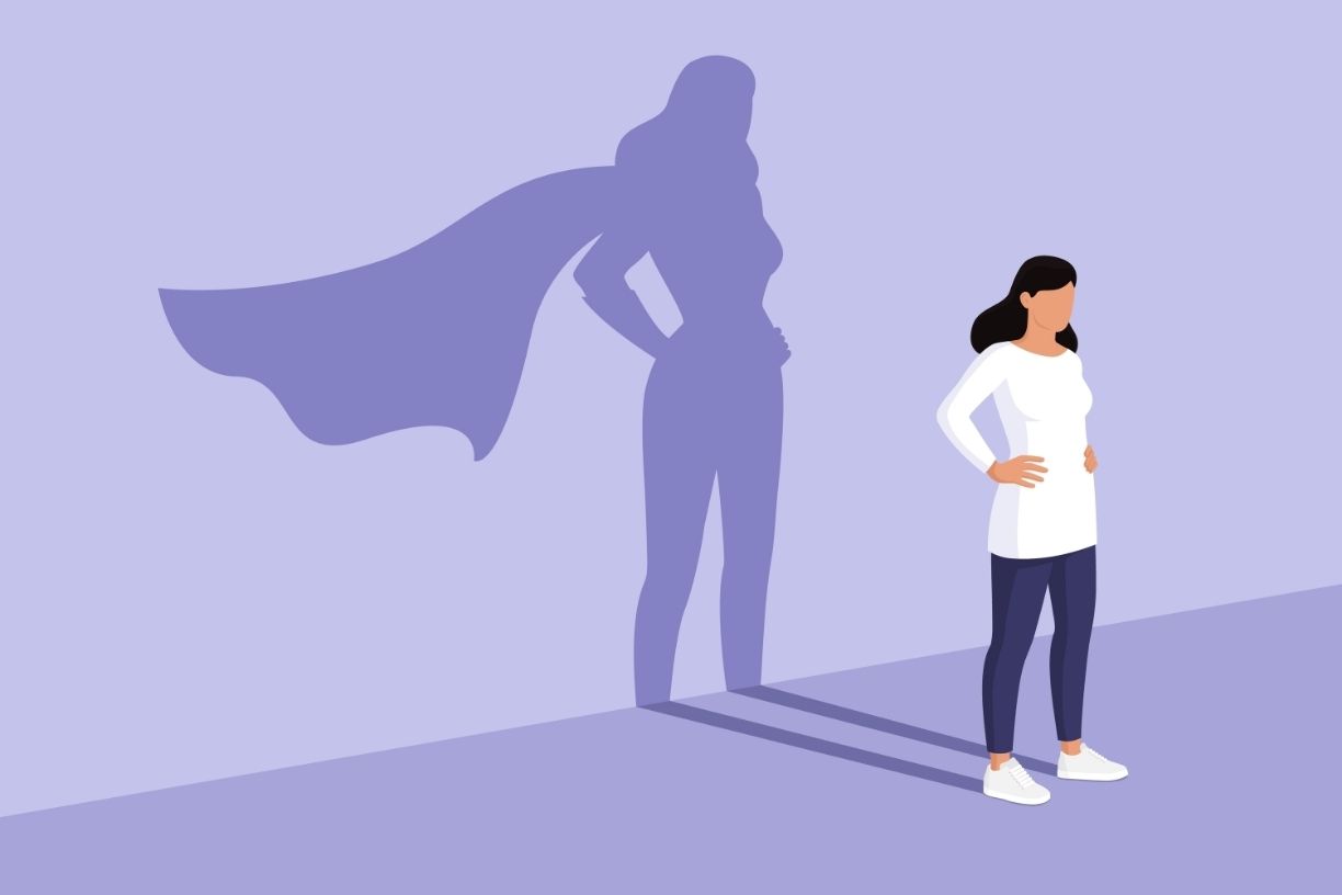 Woman standing proudly with hands on hips with her shadow adding a flowing superhero cape to represent empowered women