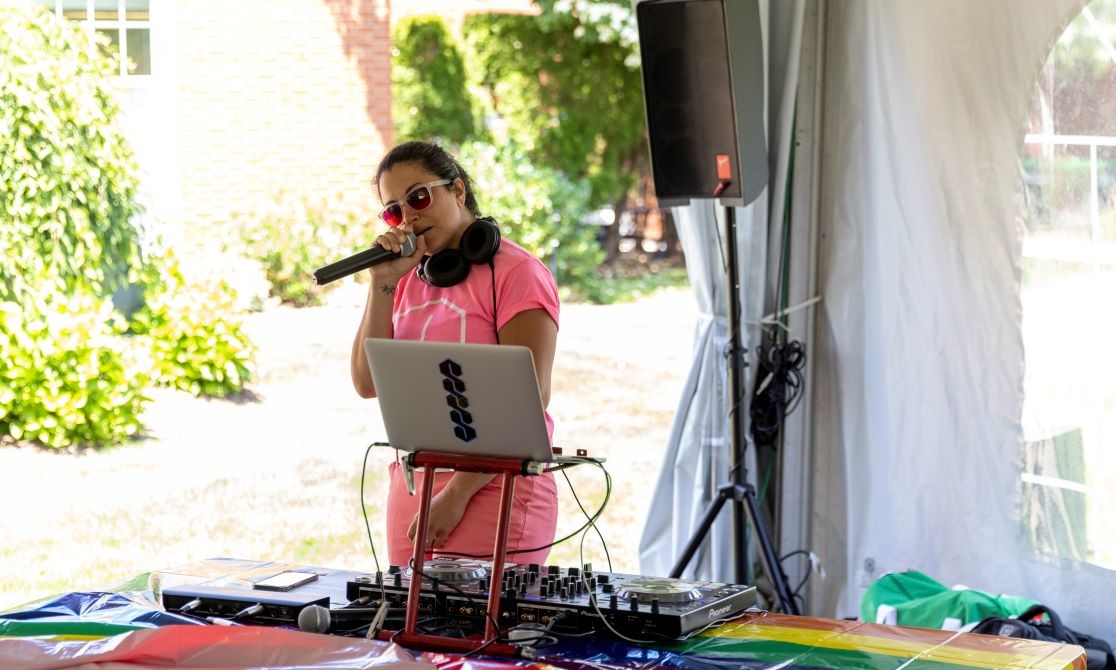 DJ wearing sunglasses holding microphone in front of a table with a rainbow tablecloth