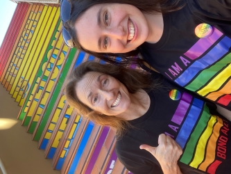 Bentley alumna and Bond University professor Amy Kenworthy poses with her daughter, Mariel Kenworthy U'Ren, in front of a stairwell painted with rainbow colors and emblazoned with the message, "Everyone is welcome here."