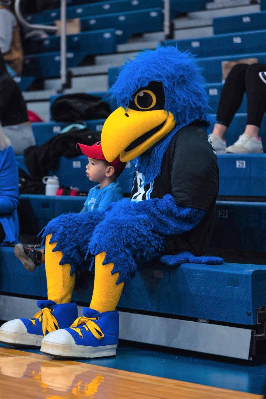 Flex the Falcon mascot sitting in bleachers next to a boy