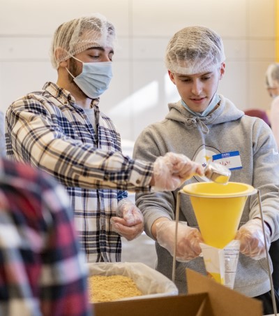 Two male Bentley students fill bags with nonperishable foods.