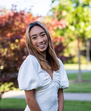 Kimiya Kim '22 wearing a white blouse standing in front of trees on campus