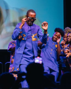 Kweku Ashiagbor dressed in blue suit and sunglasses dancing on a stage