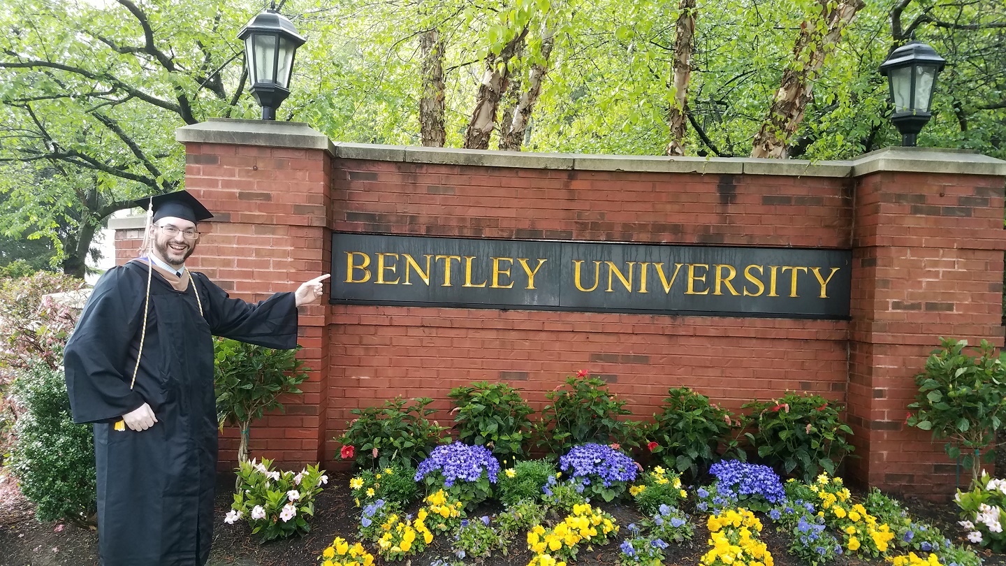 Bentley University graduate Mark Hodgdon points to the Bentley sign