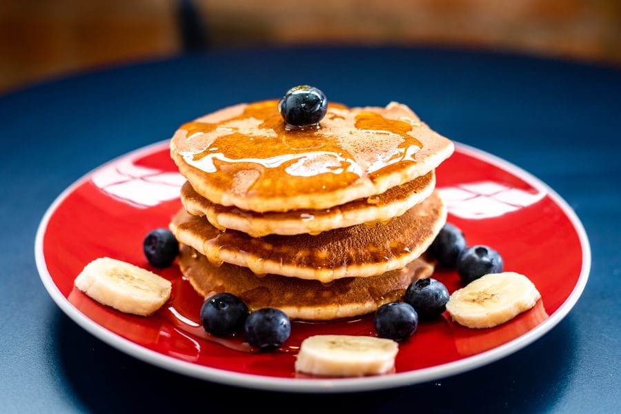 Stack of pancakes served with blueberry and banana, layered with maple syrup