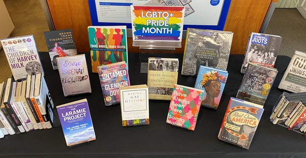books and DVDs displayed on a table with a LGBTQ+ Pride Month sign