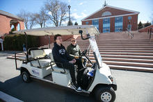 Two people sit in a golf cart in front of the Bentley Library