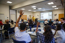 Two students raising their hands and being called on by a presenter.