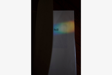 photo of an open book in deep shadow, a light rainbow falls across the page, the word Still appears in the center