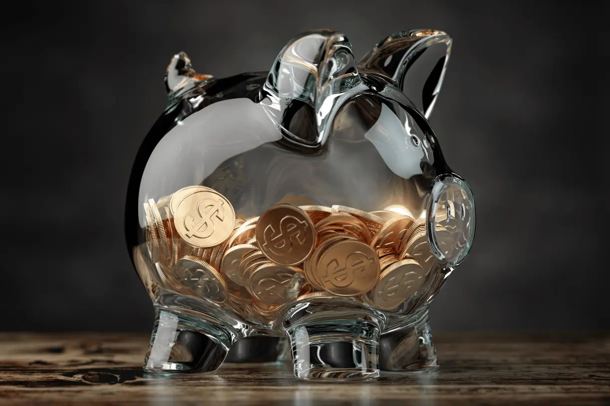 Photo of clear glass piggy bank filled halfway with gold coins.