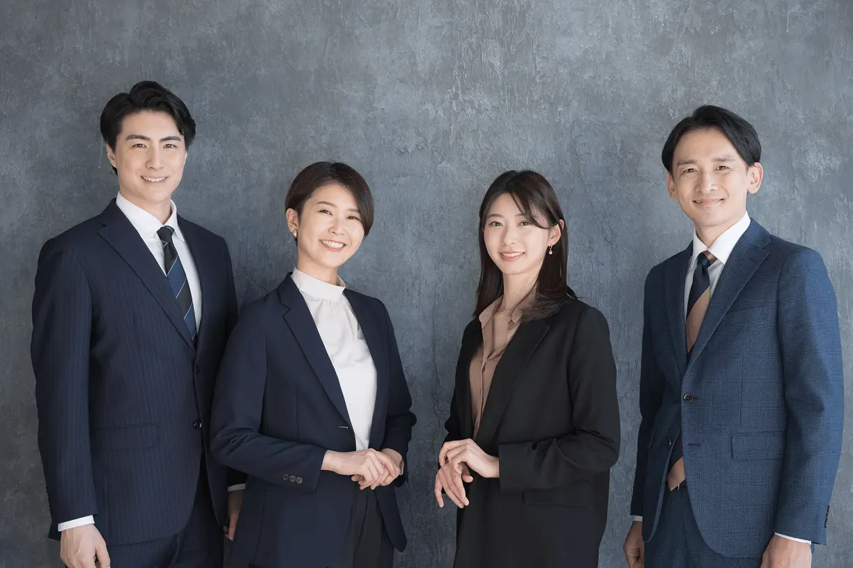 Photo of two young Asian women flanked by two young Asian men, all wearing business suits.