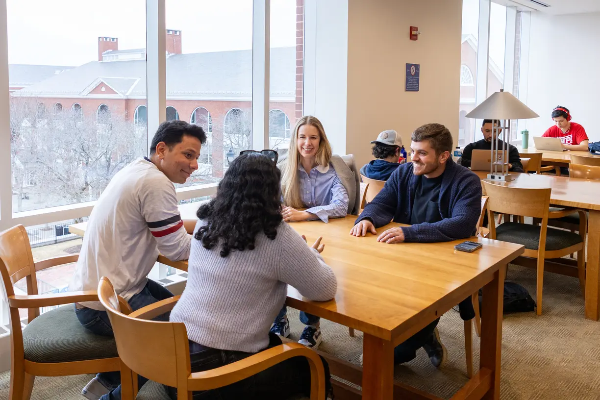 A group of Bentley graduate students conversing at a table on campus