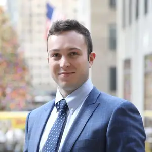 Nick Plate ’17 in suit standing in front of office building