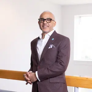 Portrait of Bentley University President E. LaBrent Chrite standing in front of a railing with a window in the background