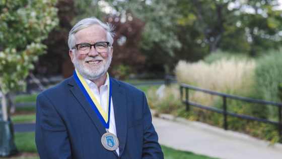 Professor Bill Gribbons poses with the medal for the 2022 Adamian Award for Lifetime Teaching Excellence on a ribbon around his neck.