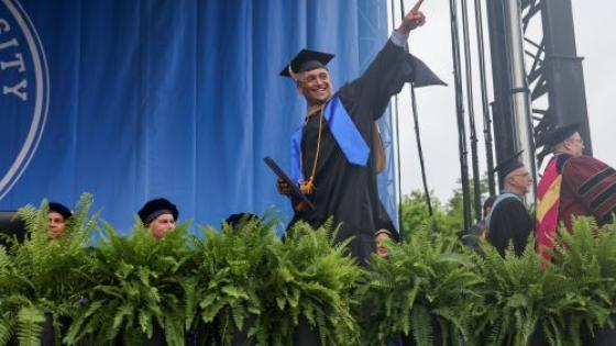 A Class of 2023 graduate walks across the stage pointing in the air