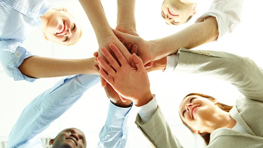 People smiling with all hands in an overlapping circle supporting each other