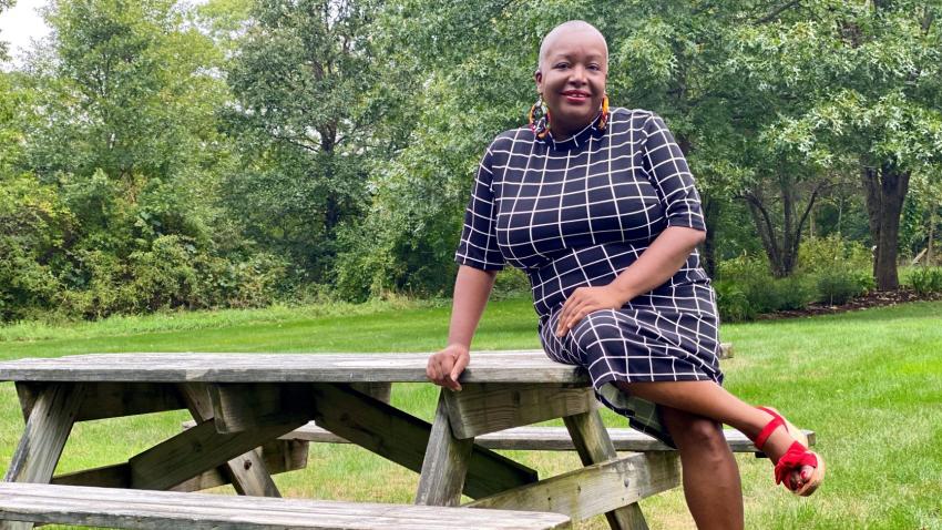 Elaine Dickson MBA'98 smiling and sitting outside on a picnic table in black and white dress