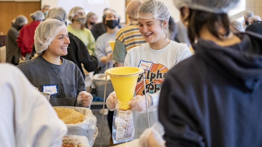 Two female Bentley students package meals during the Interfaith Council's annual Day of Service.
