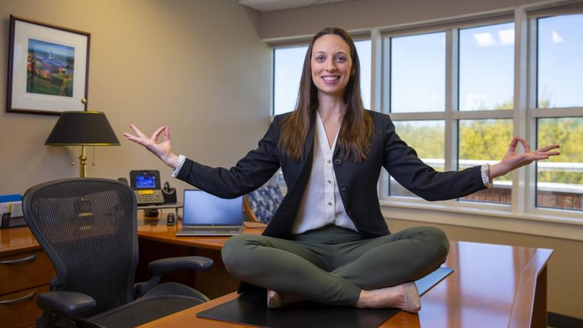 Bentley graduate sitting on the top of desk in lotus position