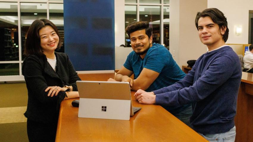 Graduate students Alice Zhang, Abhijit Chandrasekhar and Jose Ordaz stand around a laptop computer in the Bentley Library.