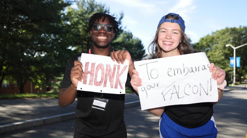 Two Bentley students holding "honk to embarrass your Falcon" signs