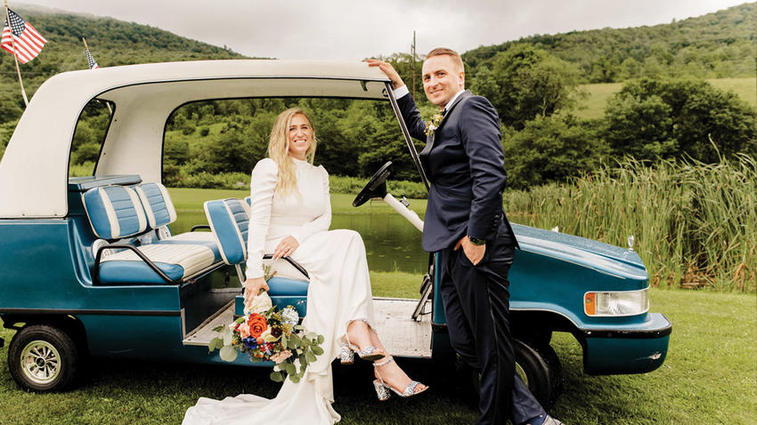 a couple poses with a car for a wedding photo