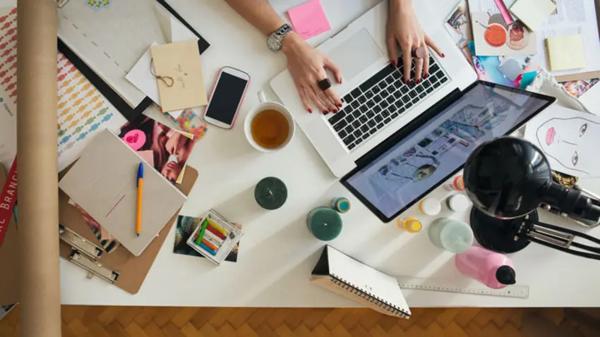 Ariel view of a cluttered table and someone typing on a laptop.