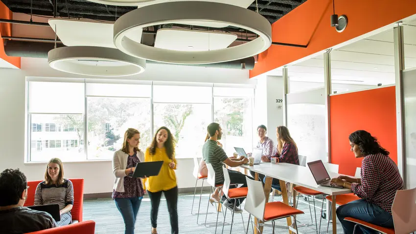 two women walk through office space looking at laptop