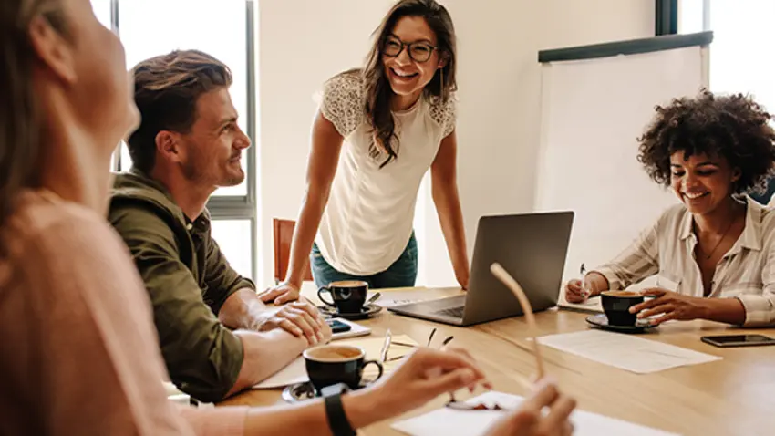Woman standing over a laptop talking to a group of people.
