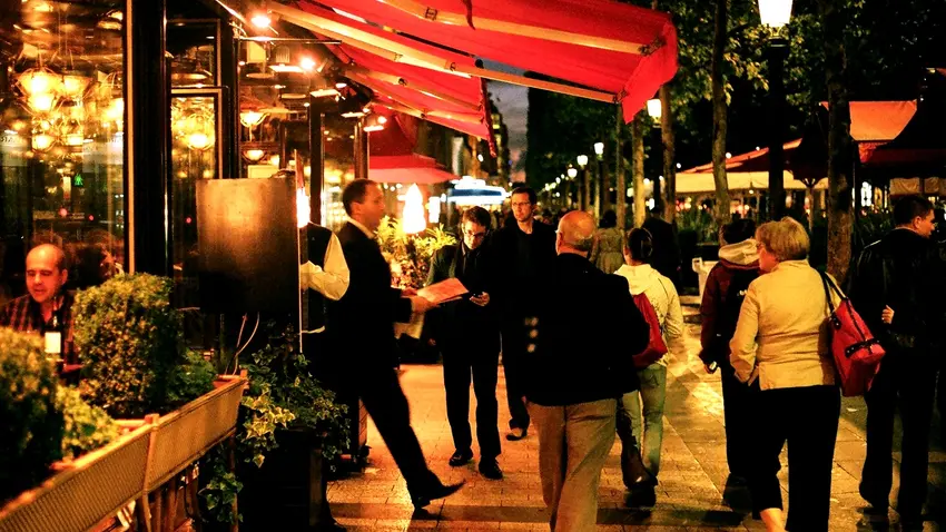People walking on the sidewalk outside of a nice restaurant.  
