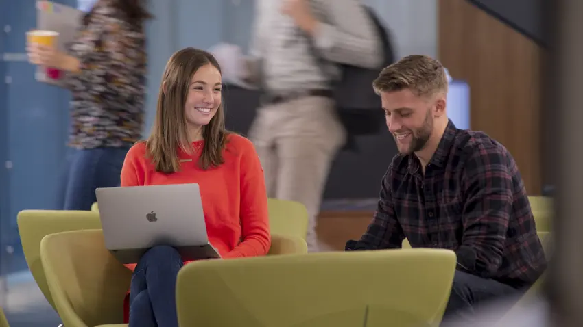 Two students sitting and conversing with students walking in background