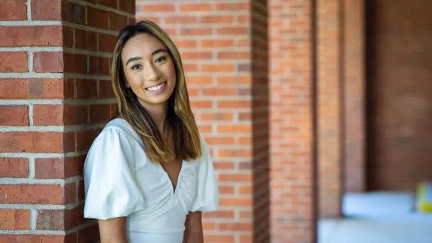 Kimiya Kim '22 wearing white blouse and standing outside in front of a brick building on campus
